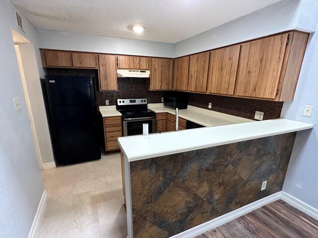 2510 Grants Lake Blvd Unit 101, Sugar Land, TX 77479 - kitchen with stainless steel electric stove, freestanding refrigerator, under cabinet range hood, brown cabinets, and light countertops