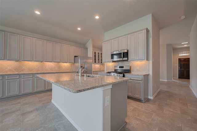 8326 Erasmus Landing Ct, Houston, TX 77044 - kitchen with appliances with stainless steel finishes, gray cabinets, tasteful backsplash, light stone counters, and a center island with sink