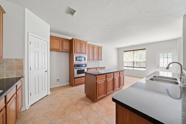 2022 Grand Willow Ln, Richmond, TX 77469 - kitchen featuring appliances with stainless steel finishes, a center island, dark countertops, brown cabinetry, and backsplash