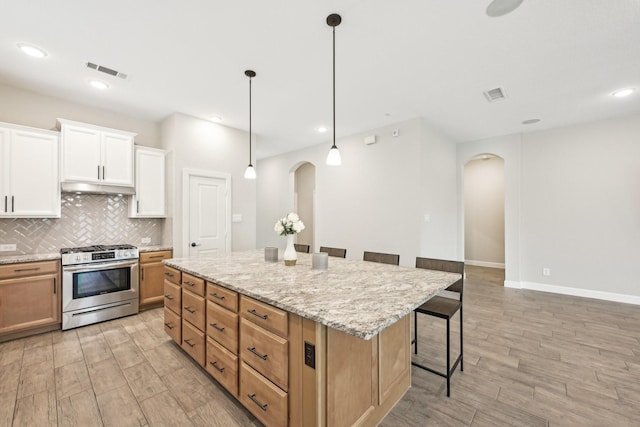 18314 Pedernales Springs Dr, Cypress, TX 77433 - kitchen with arched walkways, stainless steel range with gas stovetop, a breakfast bar area, light wood finished floors, and recessed lighting