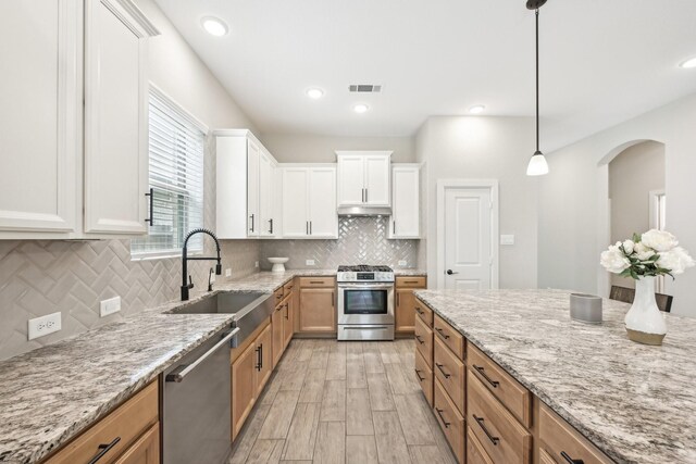18314 Pedernales Springs Dr, Cypress, TX 77433 - kitchen featuring appliances with stainless steel finishes, arched walkways, light stone countertops, decorative backsplash, and white cabinetry