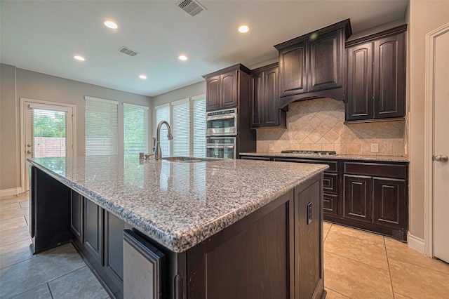 10022 Foggy Riv, Missouri City, TX 77459 - kitchen featuring recessed lighting, decorative backsplash, light stone counters, a center island with sink, and dark brown cabinetry