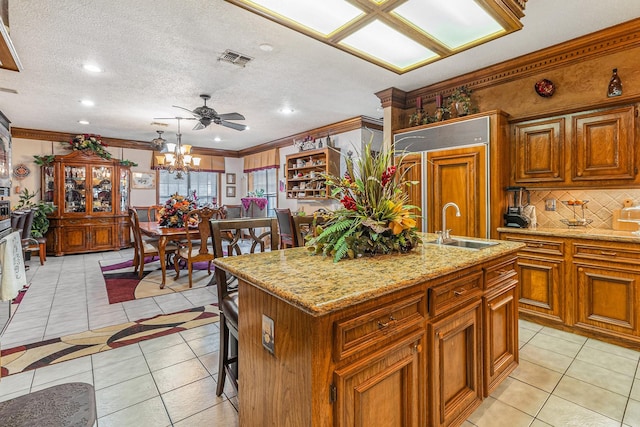 1454 Oday, Pearland, TX 77581 - kitchen featuring decorative backsplash, light tile patterned floors, a kitchen island with sink, brown cabinetry, and crown molding
