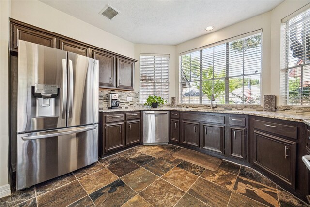 16063 Hidden Acres Dr, Houston, TX 77084 - kitchen featuring appliances with stainless steel finishes, dark brown cabinetry, stone tile flooring, backsplash, and light stone countertops
