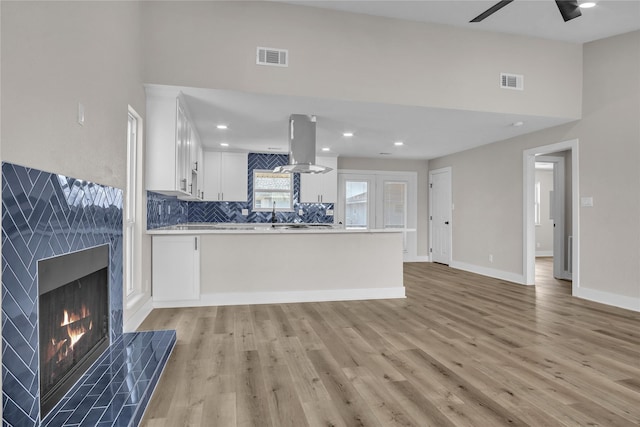 38 N Flamingo St, La Marque, TX 77568 - kitchen with island exhaust hood, light wood-style floors, ceiling fan, white cabinetry, and a high end fireplace