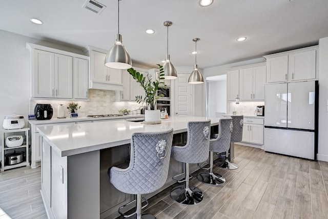 11314 Cosmopolitan Dr, Cypress, TX 77433 - kitchen with freestanding refrigerator, tasteful backsplash, light wood-type flooring, light countertops, and a kitchen island with sink