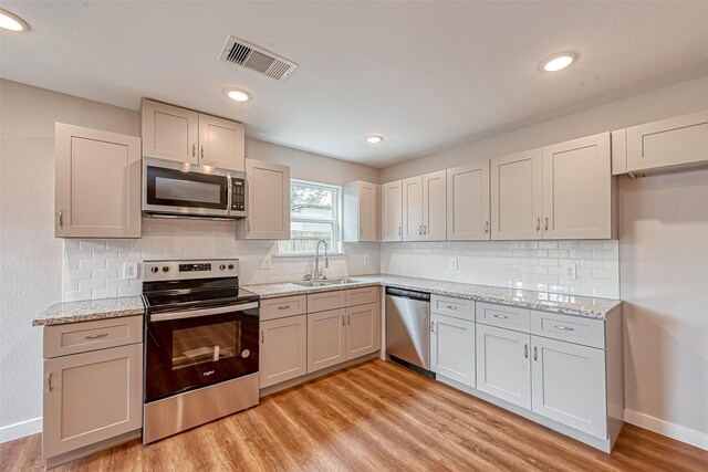 8125 Eastover St Unit Ab, Houston, TX 77028 - kitchen featuring stainless steel appliances, light wood-type flooring, decorative backsplash, light stone counters, and recessed lighting