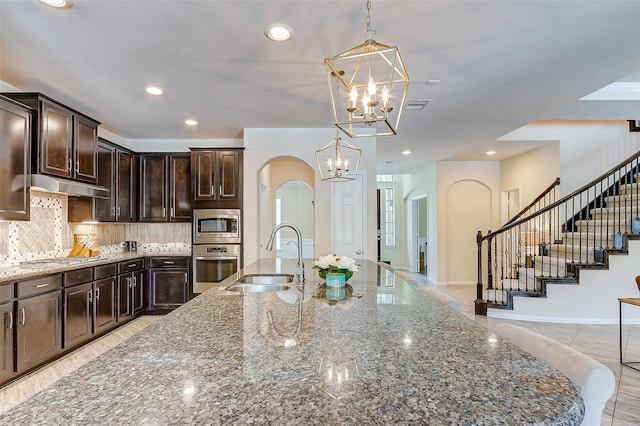 20910 Cordell Landing Dr, Richmond, TX 77407 - kitchen with appliances with stainless steel finishes, arched walkways, tasteful backsplash, dark stone counters, and a chandelier