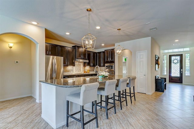 20910 Cordell Landing Dr, Richmond, TX 77407 - kitchen with appliances with stainless steel finishes, arched walkways, dark stone counters, dark brown cabinetry, and tasteful backsplash