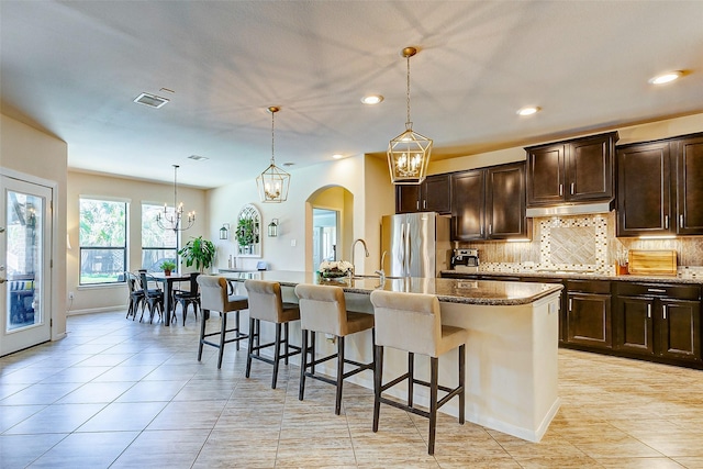 20910 Cordell Landing Dr, Richmond, TX 77407 - kitchen with freestanding refrigerator, an island with sink, tasteful backsplash, arched walkways, and a breakfast bar area