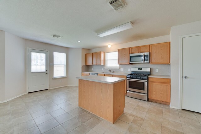 2614 Skyview Shadows Ct, Houston, TX 77047 - kitchen with appliances with stainless steel finishes, a center island, light countertops, light tile patterned floors, and a textured ceiling