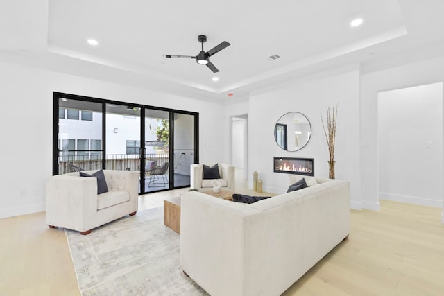 5115 Maple St, Houston, TX 77401 - living room with a tray ceiling, light wood-style flooring, recessed lighting, a glass covered fireplace, and ceiling fan