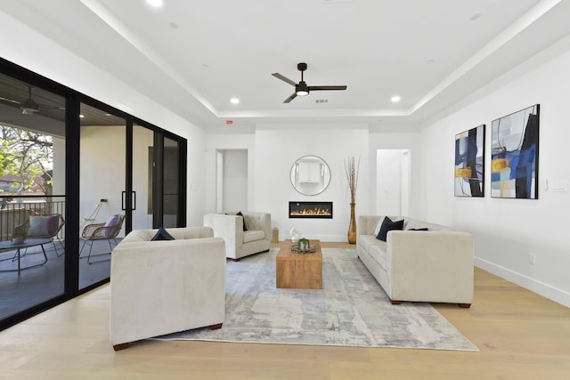 5115 Maple St, Houston, TX 77401 - living room with a ceiling fan, a tray ceiling, light wood-style floors, a glass covered fireplace, and recessed lighting