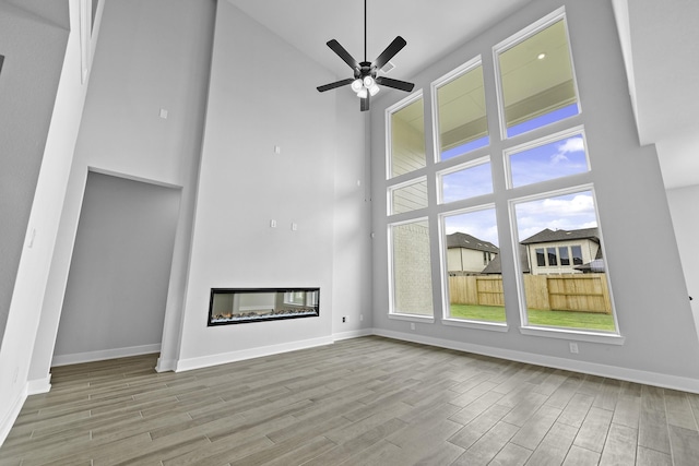 3244 Stingray Cove Dr, Katy, TX 77493 - unfurnished living room with a high ceiling, wood finished floors, ceiling fan, and a glass covered fireplace