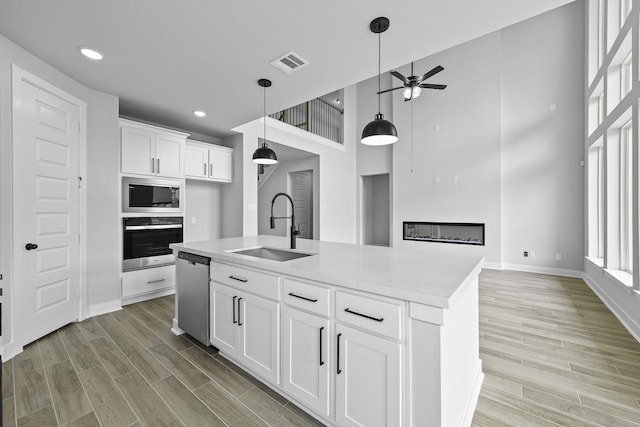 3244 Stingray Cove Dr, Katy, TX 77493 - kitchen with stainless steel appliances, a ceiling fan, white cabinets, light countertops, and light wood-type flooring