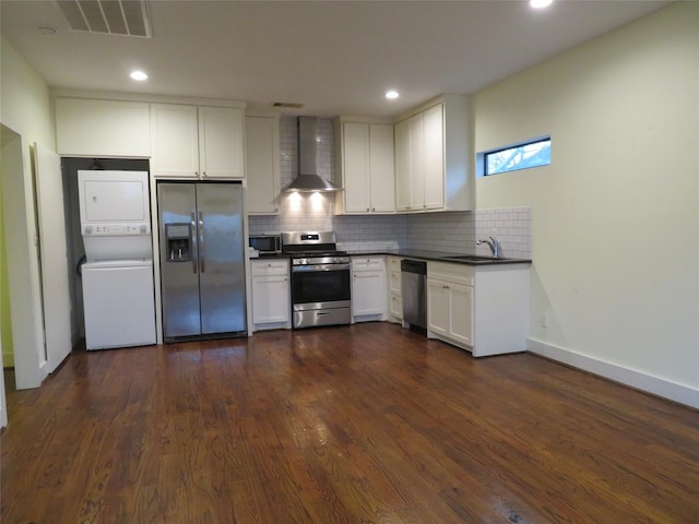 4730 Bell St, Houston, TX 77023 - kitchen with appliances with stainless steel finishes, wall chimney exhaust hood, stacked washer and clothes dryer, dark countertops, and tasteful backsplash
