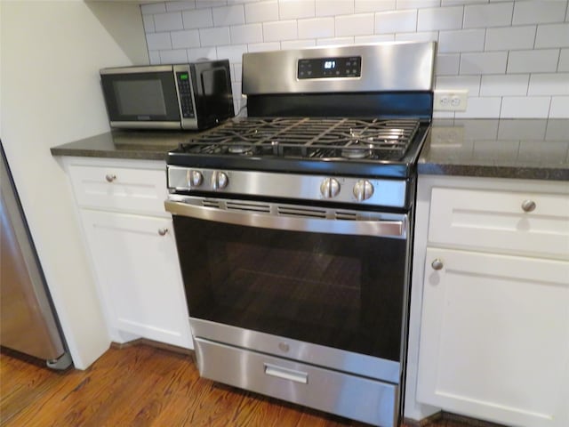4730 Bell St, Houston, TX 77023 - kitchen featuring appliances with stainless steel finishes, backsplash, white cabinets, dark wood-style floors, and dark stone countertops
