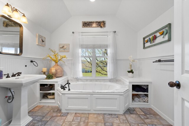34210 Sanders Ranch Rd, Magnolia, TX 77355 - bathroom featuring a garden tub, wainscoting, vaulted ceiling, and stone finish floors
