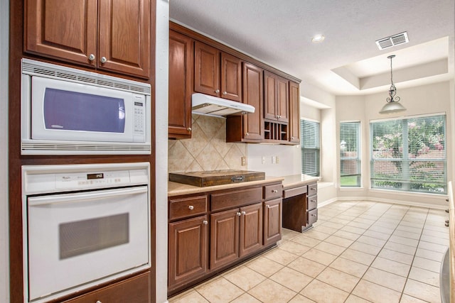 24006 Northshire Ln, Katy, TX 77494 - kitchen with white appliances, under cabinet range hood, light tile patterned flooring, backsplash, and decorative light fixtures