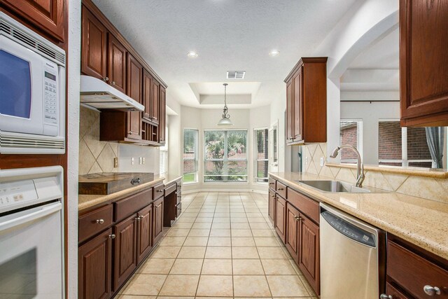 24006 Northshire Ln, Katy, TX 77494 - kitchen featuring white appliances, a raised ceiling, tasteful backsplash, under cabinet range hood, and light tile patterned flooring