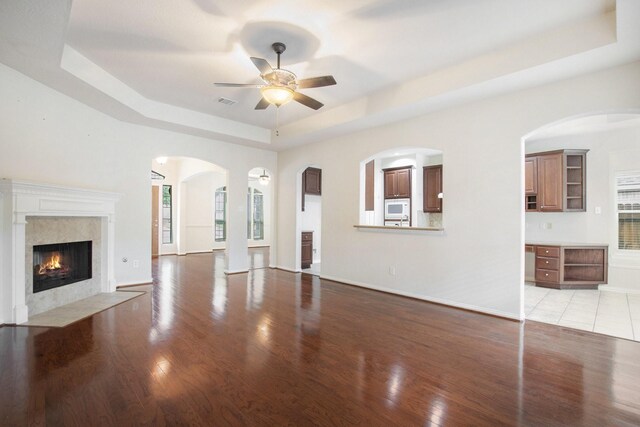 24006 Northshire Ln, Katy, TX 77494 - unfurnished living room featuring a tray ceiling, light wood finished floors, a ceiling fan, a fireplace, and healthy amount of natural light