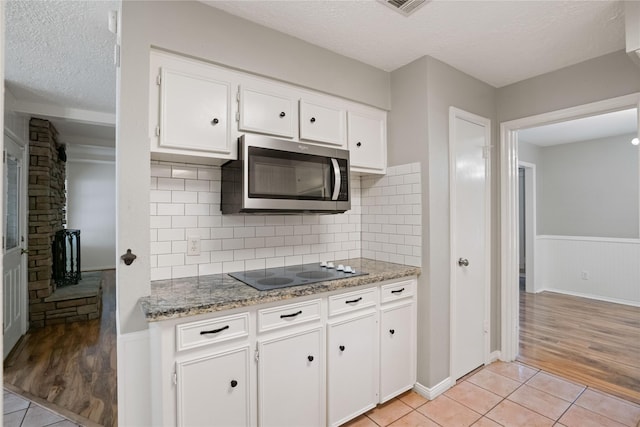8214 Camborne Ln, Houston, TX 77070 - kitchen with stainless steel microwave, electric cooktop, a textured ceiling, white cabinetry, and light tile patterned floors