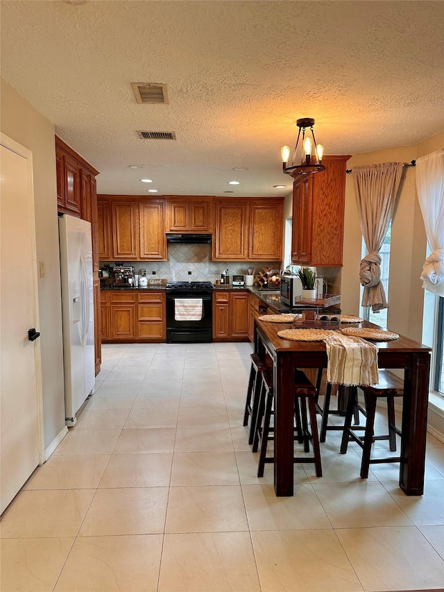 5103 Kleinbrook Dr, Houston, TX 77066 - kitchen featuring white refrigerator with ice dispenser, black gas stove, dark countertops, under cabinet range hood, and decorative backsplash