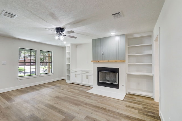 707 N Main St, Dayton, TX 77535 - unfurnished living room with a textured ceiling, a ceiling fan, a large fireplace, light wood-style flooring, and baseboards