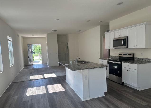 12614 Galatea, San Antonio, TX 78245 - kitchen featuring stainless steel appliances, dark wood-style flooring, white cabinets, a kitchen island with sink, and dark stone counters