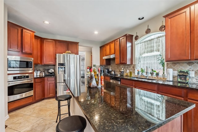 3318 Legends Mist Dr, Spring, TX 77386 - kitchen featuring appliances with stainless steel finishes, tasteful backsplash, a kitchen breakfast bar, dark stone counters, and under cabinet range hood