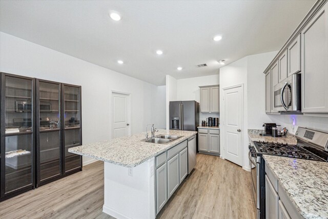 7227 Songlark Landing Ct, Katy, TX 77493 - kitchen featuring appliances with stainless steel finishes, gray cabinetry, light wood-style flooring, light stone counters, and a kitchen island with sink