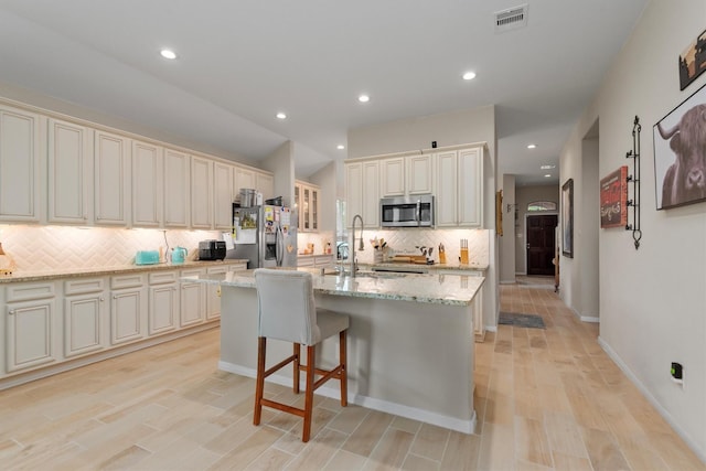 9171 White Tail Dr, Conroe, TX 77303 - kitchen with appliances with stainless steel finishes, cream cabinetry, tasteful backsplash, light stone countertops, and a center island with sink