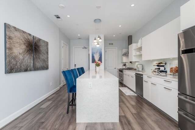 1211 Caroline St Unit 1504, Houston, TX 77002 - kitchen featuring appliances with stainless steel finishes, a center island, wall chimney exhaust hood, dark wood-type flooring, and white cabinetry