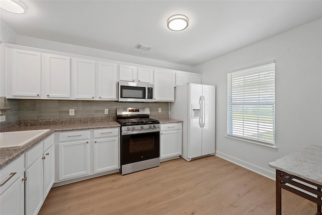 206 Delaney St, Houston, TX 77009 - kitchen with appliances with stainless steel finishes, decorative backsplash, light wood-style floors, and white cabinets