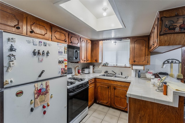 7726 Melanie St, Houston, TX 77016 - kitchen featuring freestanding refrigerator, gas range, black microwave, light tile patterned floors, and brown cabinets