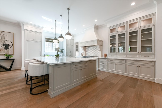 3028 Locke Ln, Houston, TX 77019 - kitchen with premium range hood, light countertops, a center island with sink, crown molding, and light wood finished floors