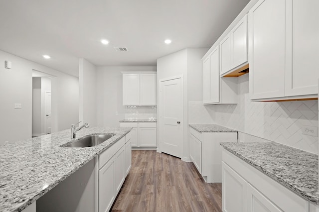 25017 Pomegranate Pl, Montgomery, TX 77316 - kitchen with light wood-style flooring, light stone counters, backsplash, recessed lighting, and white cabinetry