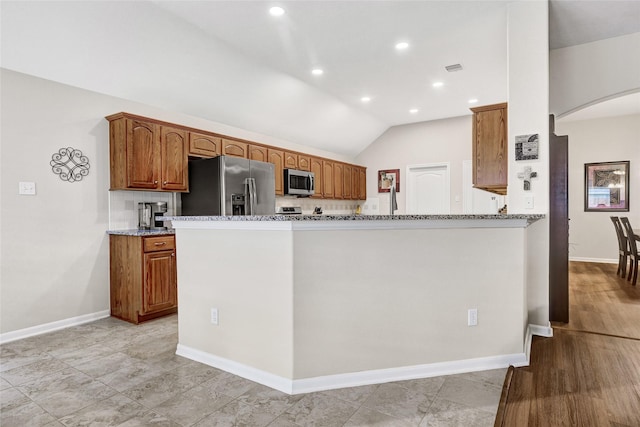 6318 Crystal Forest Trl, Katy, TX 77493 - kitchen featuring stainless steel appliances, arched walkways, light stone countertops, lofted ceiling, and brown cabinetry
