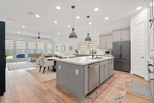 16903 Lupine Meadow Ln, Humble, TX 77346 - kitchen featuring stainless steel appliances, gray cabinetry, light countertops, light wood-style floors, and a kitchen island with sink