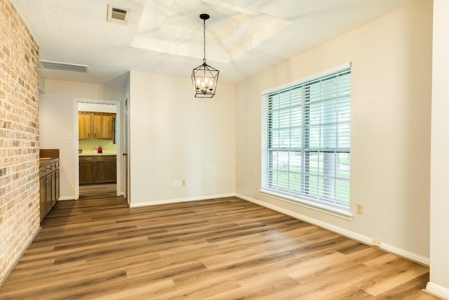 2910 Castle Ct, Pearland, TX 77581 - unfurnished dining area with light wood-type flooring, a tray ceiling, a chandelier, and brick wall