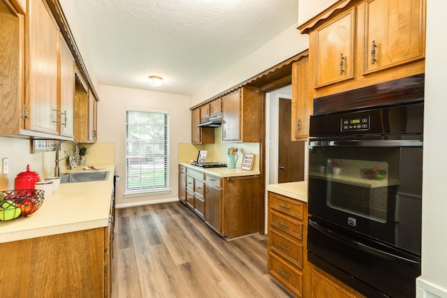 2910 Castle Ct, Pearland, TX 77581 - kitchen featuring a warming drawer, black oven, under cabinet range hood, light wood finished floors, and brown cabinetry