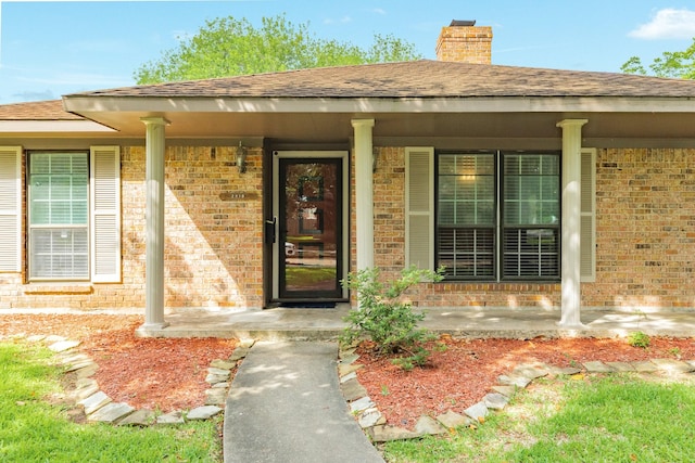 2910 Castle Ct, Pearland, TX 77581 - view of exterior entry with brick siding, a chimney, a porch, and roof with shingles