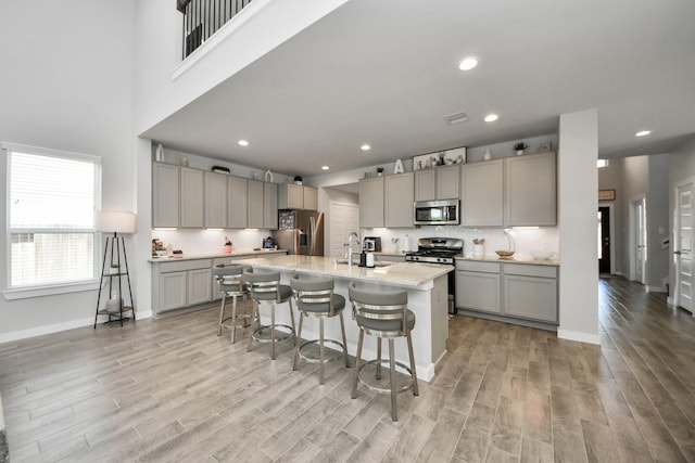 3334 Fogmist Dr, Rosenberg, TX 77471 - kitchen with stainless steel appliances, gray cabinetry, light wood-style flooring, a breakfast bar area, and an island with sink