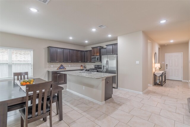 9418 Mcdowell Dr, Richmond, TX 77469 - kitchen featuring stainless steel appliances, backsplash, dark brown cabinets, a center island with sink, and light stone counters