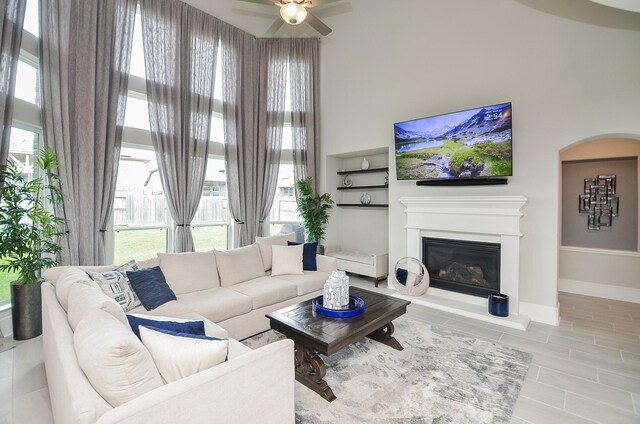 8703 Silver Crest Ln, Missouri City, TX 77459 - living area featuring a glass covered fireplace, arched walkways, ceiling fan, and a towering ceiling