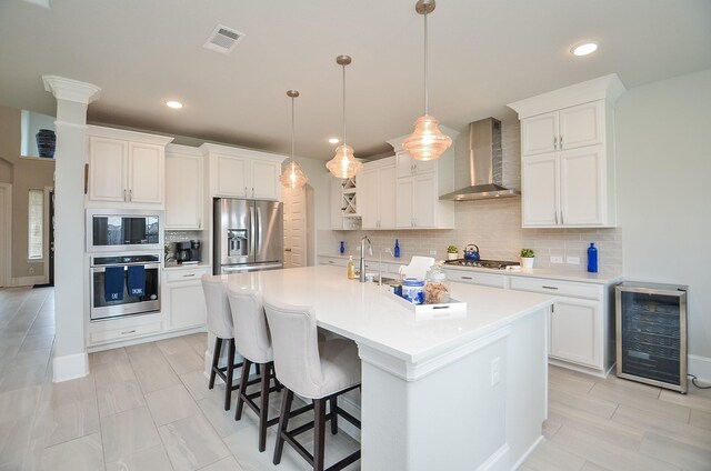8703 Silver Crest Ln, Missouri City, TX 77459 - kitchen featuring wall chimney range hood, appliances with stainless steel finishes, wine cooler, decorative backsplash, and white cabinetry