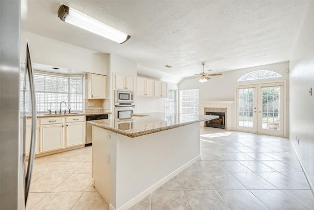 5007 Maple Brook Ln, Kingwood, TX 77345 - kitchen with appliances with stainless steel finishes, a tiled fireplace, a ceiling fan, light tile patterned floors, and light stone counters