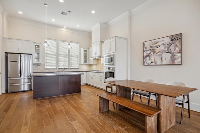 9520 London Bridge Sta, Houston, TX 77045 - kitchen featuring stainless steel appliances, glass insert cabinets, a kitchen island, wood finished floors, and ornamental molding