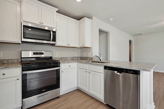 425 Tejas Trl, Waller, TX 77484 - kitchen featuring appliances with stainless steel finishes, light wood finished floors, a peninsula, and white cabinetry