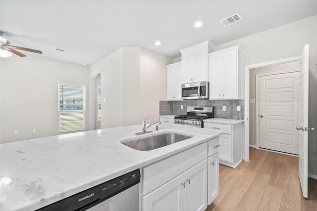 426 Emerald Thicket Ln, Huffman, TX 77336 - kitchen featuring appliances with stainless steel finishes, arched walkways, a ceiling fan, light wood-type flooring, and light stone counters